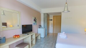 A hotel room with a bed, a desk with a television, a small refrigerator, and a mirror. - Poros Beach (Lefkada)