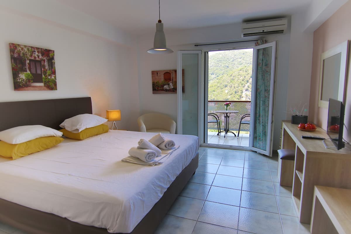 Habitación de hotel con cama, escritorio, silla, balcón con mesa y un cuadro en la pared.