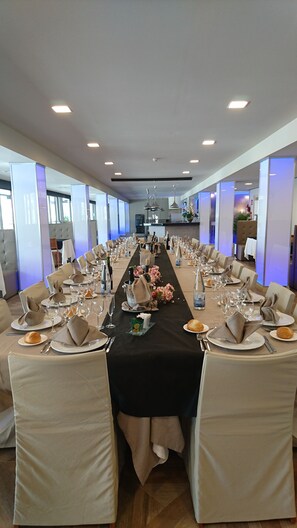 A long dining table set for a formal event with multiple chairs, a black tablecloth, and elegant table settings including wine glasses, plates, and napkins.