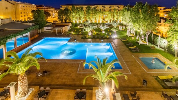 Ein Hotelpoolbereich mit mehreren Schwimmbecken, Liegestühlen und Palmen.