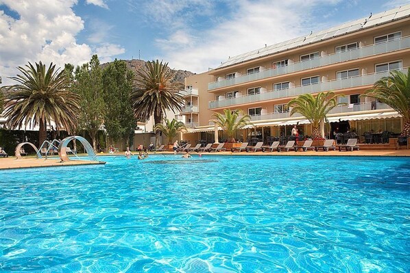 A swimming pool with lounge chairs and palm trees, surrounded by a multi-story building with balconies.