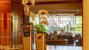 Eine Lobby mit zwei großen, spiegelnden Vasen mit Orchideen, einer Sitzecke mit Sofas und Blick ins Freie durch große Fenster.