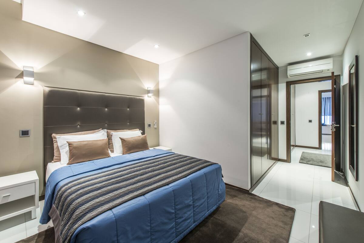 Un dormitorio moderno con una cama grande, mesitas de noche, cabecero empotrado y vestidor.
