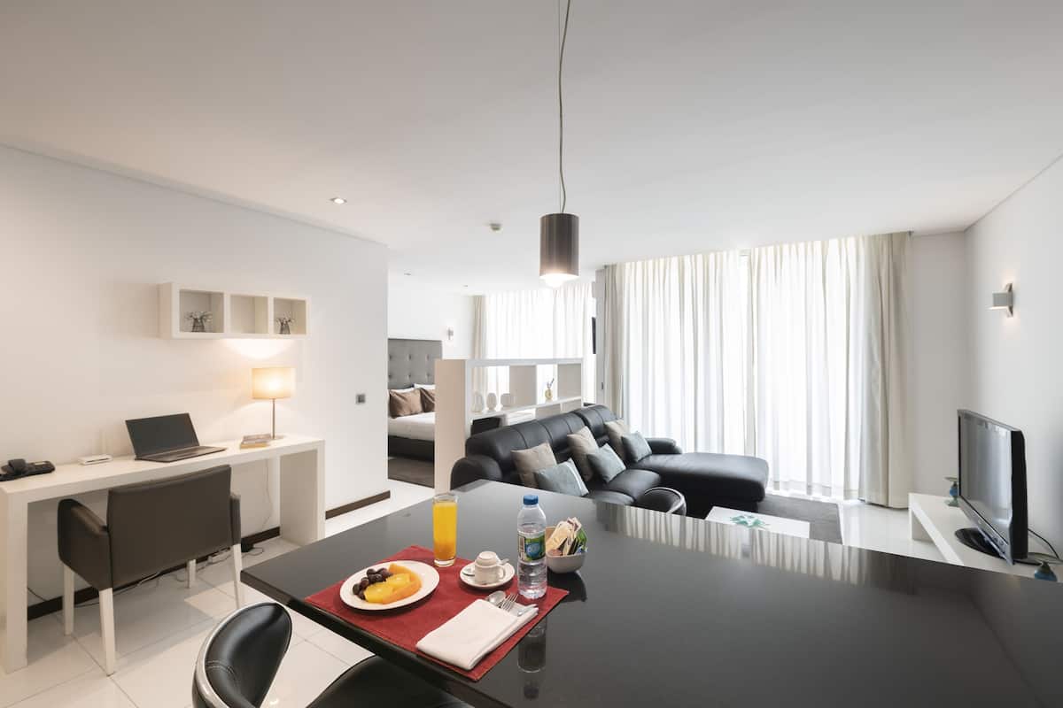 Una habitación de hotel moderna con zona de comedor, sofá, televisor y escritorio con computadora portátil.