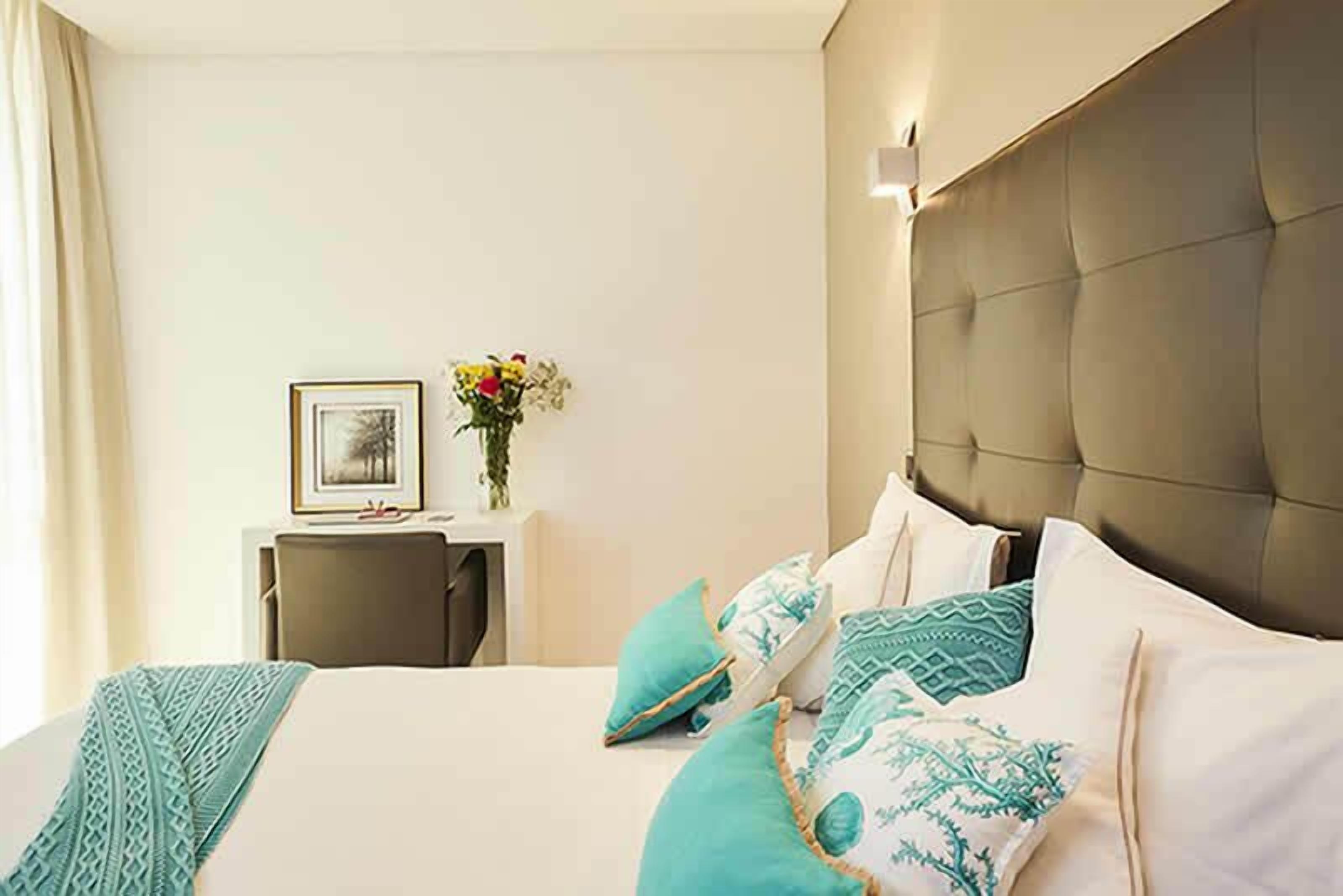 A hotel room with a large bed, a bedside table with a vase of flowers, and a framed picture on the wall.