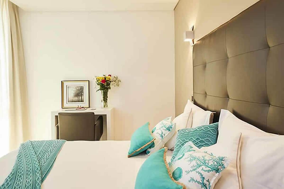 A hotel room with a large bed, a bedside table with a vase of flowers, and a framed picture on the wall.
