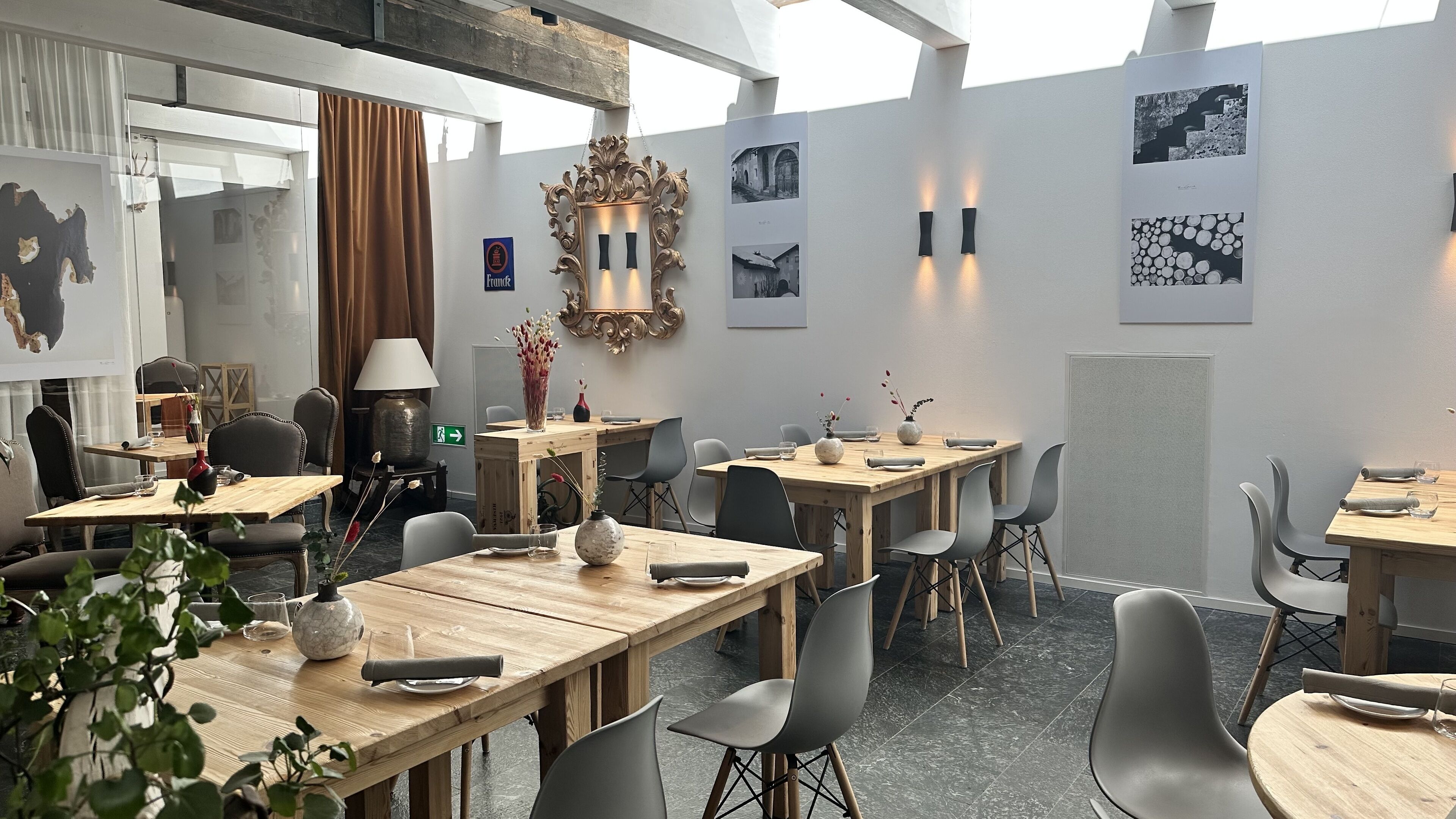 Un espace repas moderne avec des tables en bois et des chaises grises, un miroir décoratif et des tableaux encadrés accrochés aux murs.