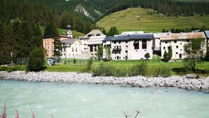 A hotel with multiple buildings, a river in the foreground, and a mountainous backdrop. - Chesa Stuva Colani (Madulain)