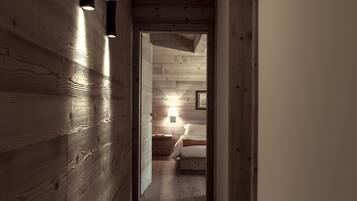 A wooden hallway with a bed in the distance, a nightstand, and a lamp.