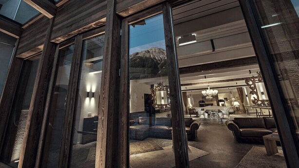 A modern interior with a large glass door leading to a living area featuring a sofa, coffee table, and dining table. - Chesa Stuva Colani (Madulain)