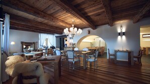 A rustic interior with wooden beams, a chandelier, and a dining area with chairs and tables. - Chesa Stuva Colani (Madulain)