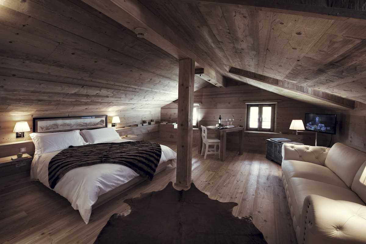 A cozy log cabin bedroom with a bed, a sofa, a desk, and a television.
