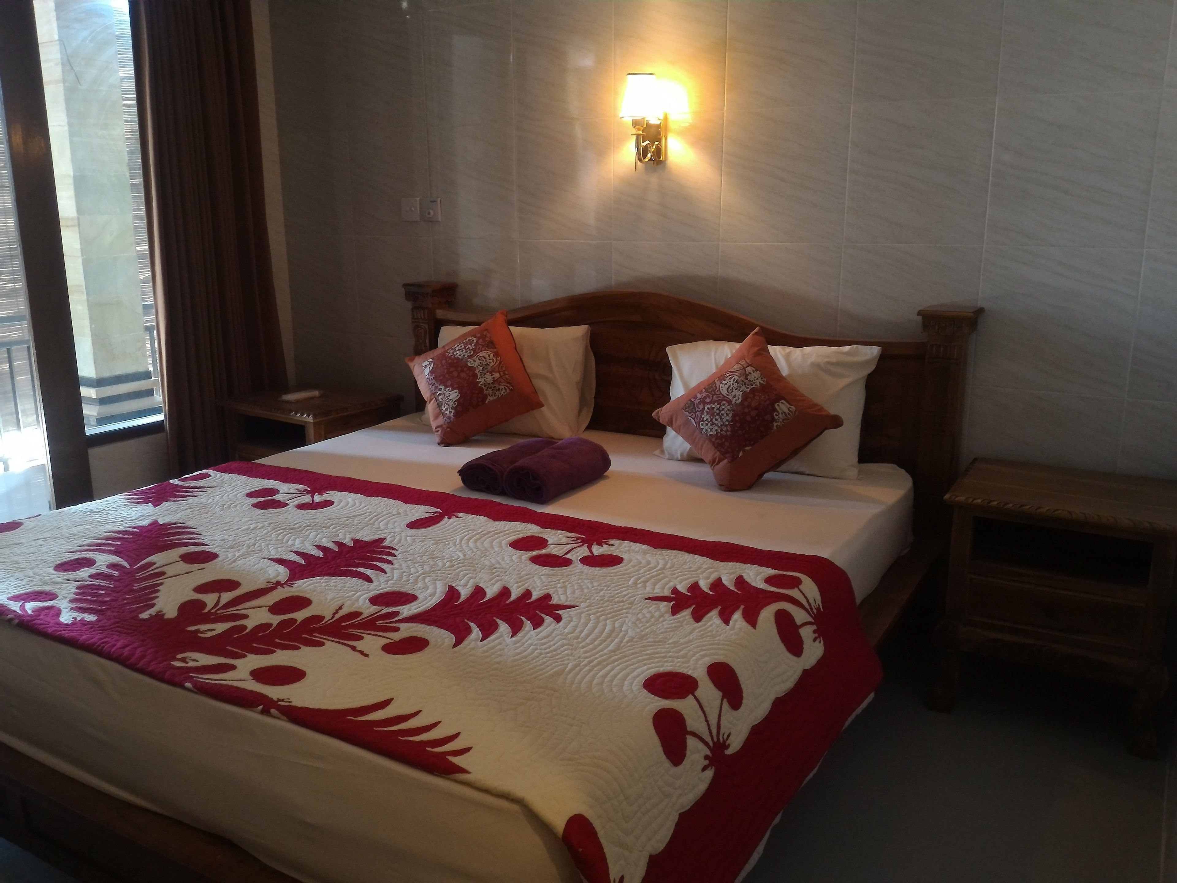 A neatly made bed with a floral-patterned bedspread, two pillows, and a bedside lamp.