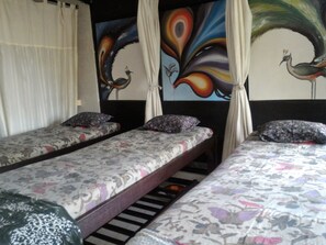 A room with two single beds, each with floral-patterned bedding and pillows. There is a curtain on one side and a wall with a peacock painting.
