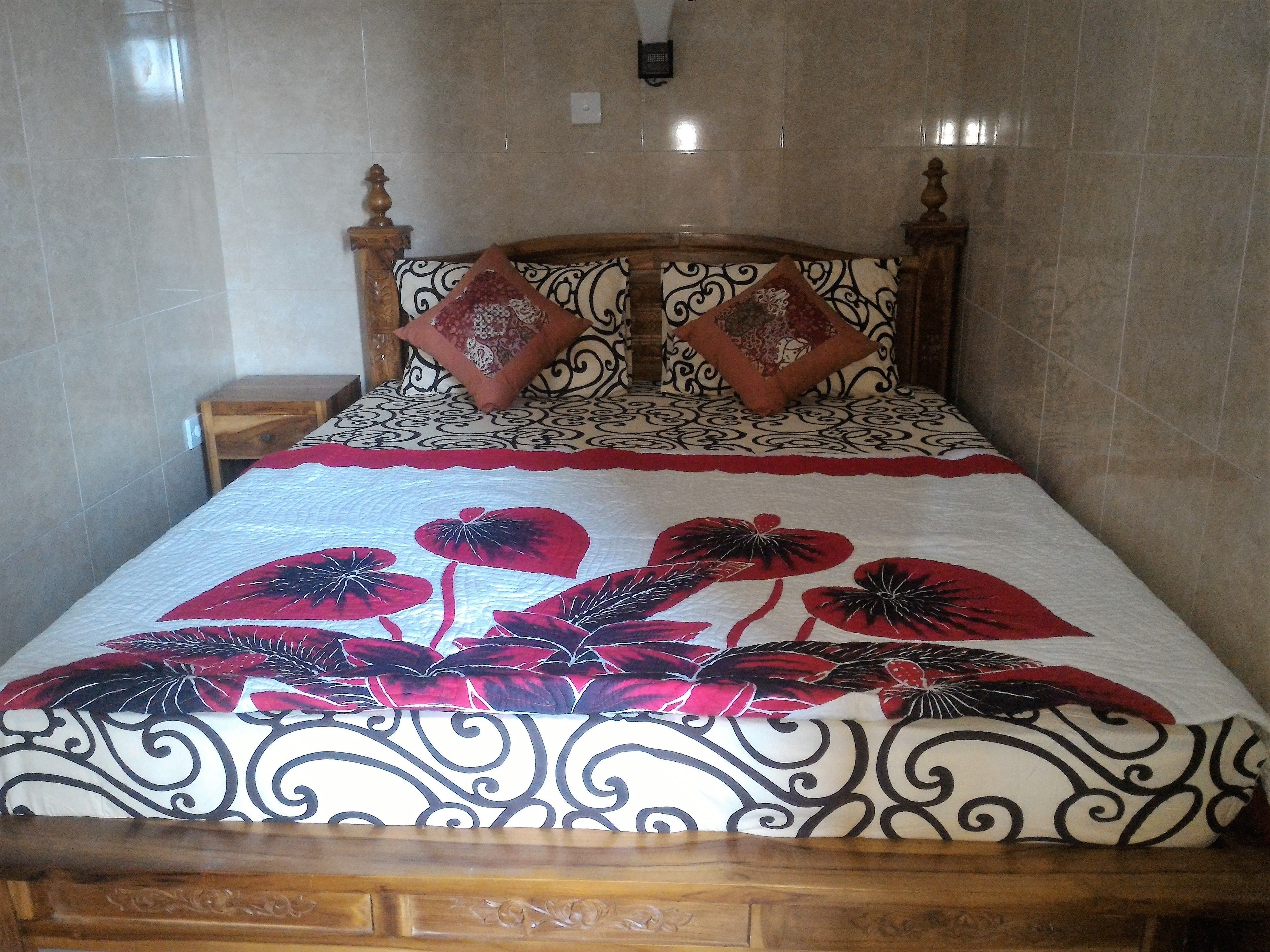 Una cama con una colcha estampada, dos almohadas decorativas y un cabecero de madera.