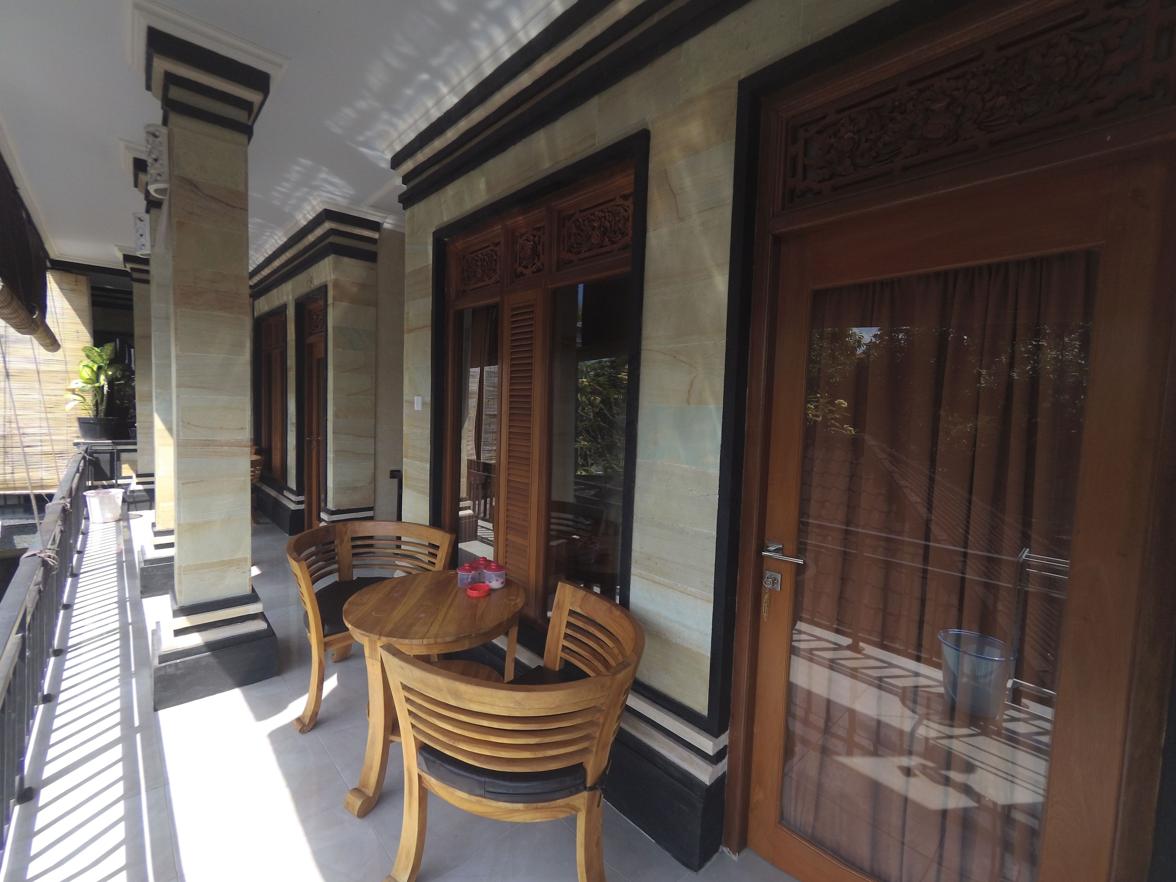 A covered outdoor seating area with two wooden tables and chairs, a potted plant, and a view of the street.