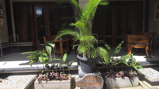 A welcome sign at the entrance of a property with potted plants and wooden furniture. - Rumah Ary Homestay & Spa (Ubud)