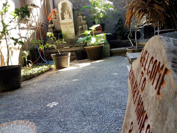 A courtyard with a stone pathway, potted plants, and a welcome sign.