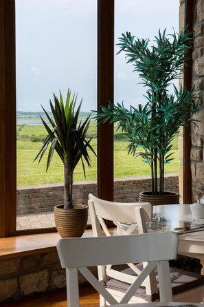 A dining area with a table and chairs, a view of the countryside through large windows, and two potted plants. - Down Yonder Boutique B&B (Rosses Point)