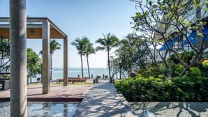 A beachfront walkway with a wooden pergola, palm trees, and a view of the ocean.