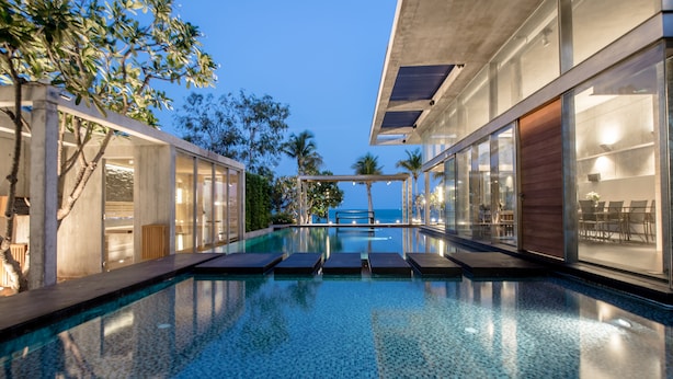 A modern infinity pool with clear blue water, surrounded by glass walls and wooden deck chairs.