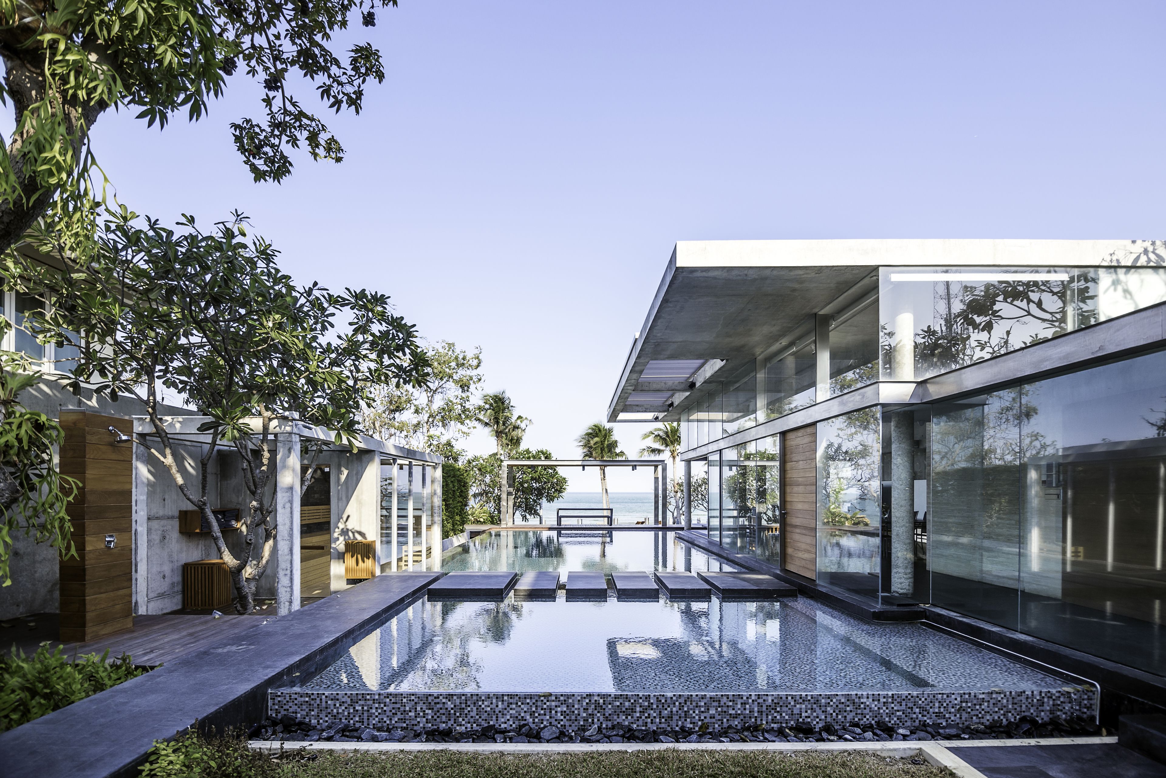 Un área de piscina moderna con paredes de vidrio y vista al mar.