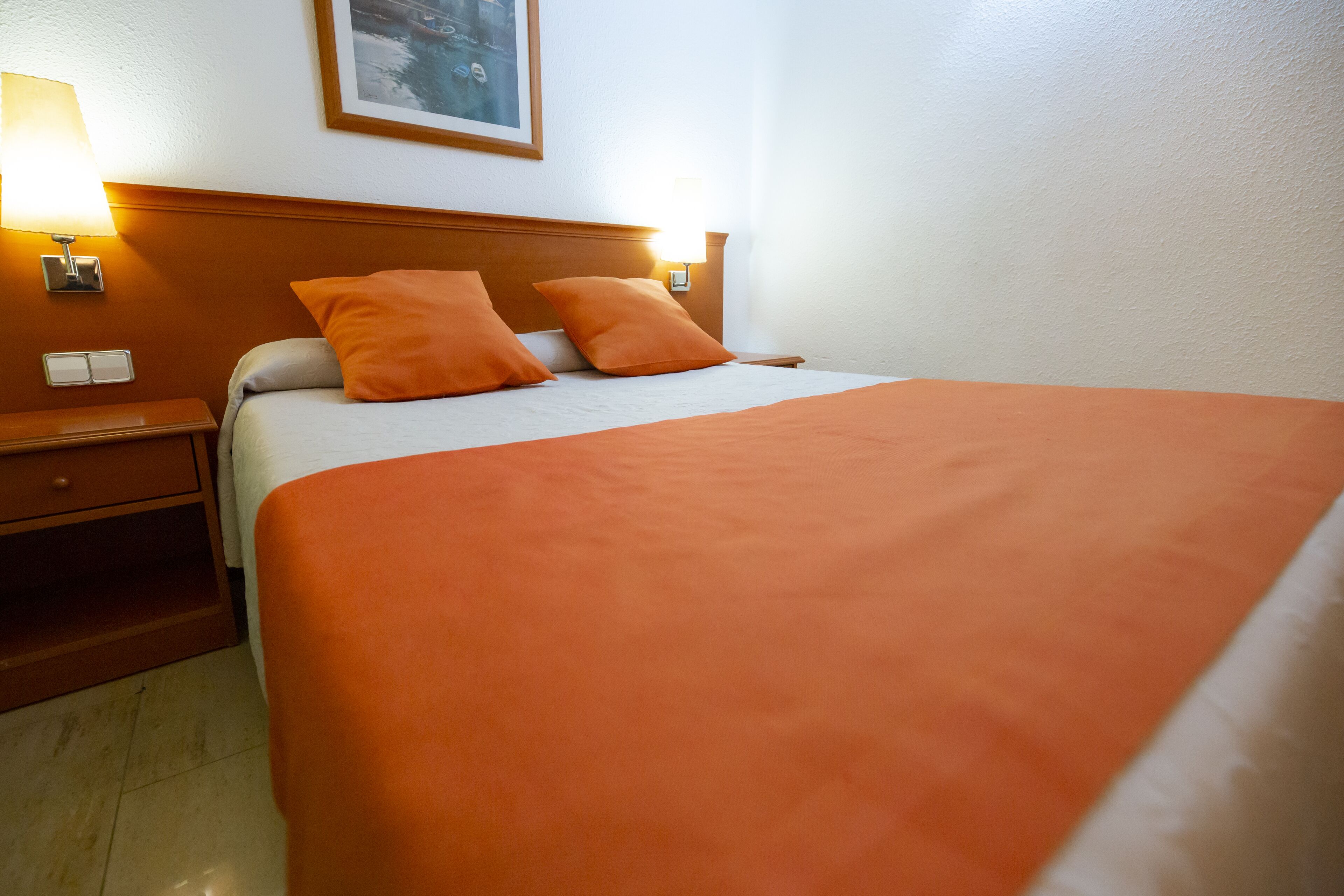 Un lit bien fait, avec une couvre-lit et des oreillers orange, une tête de lit en bois et deux lampes de chevet.