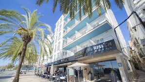 A hotel with outdoor seating, palm trees, and a clear blue sky. - Hotel Risech (Roses)