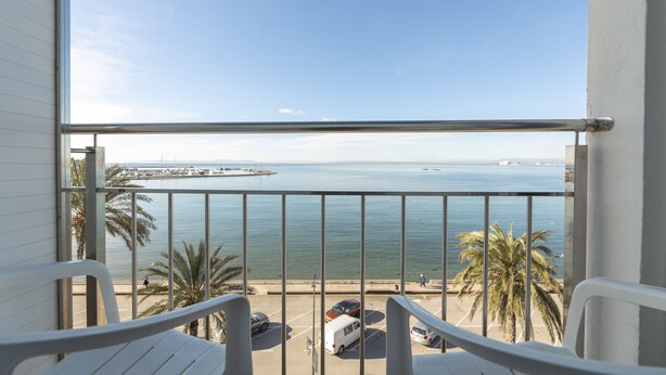 A balcony with a view of the sea, palm trees, and parked cars. - Hotel Risech (Roses)