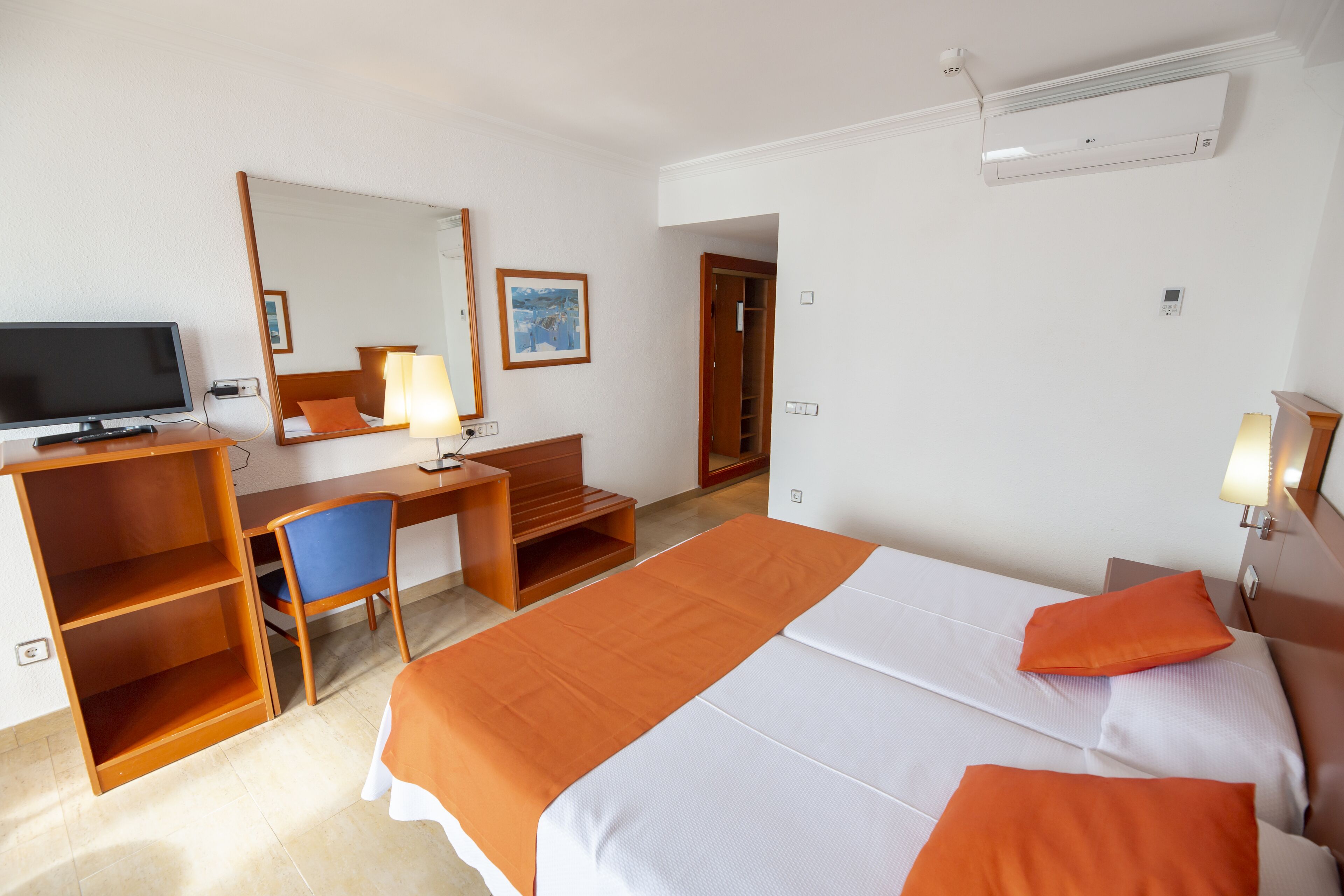 Une chambre d’hôtel équipée d’un lit, d’un bureau, d’une chaise, d’une télévision et d’un miroir.