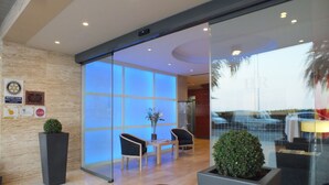 A hotel lobby with a reception desk, seating area, and a glass entrance. - Hotel Risech (Roses)
