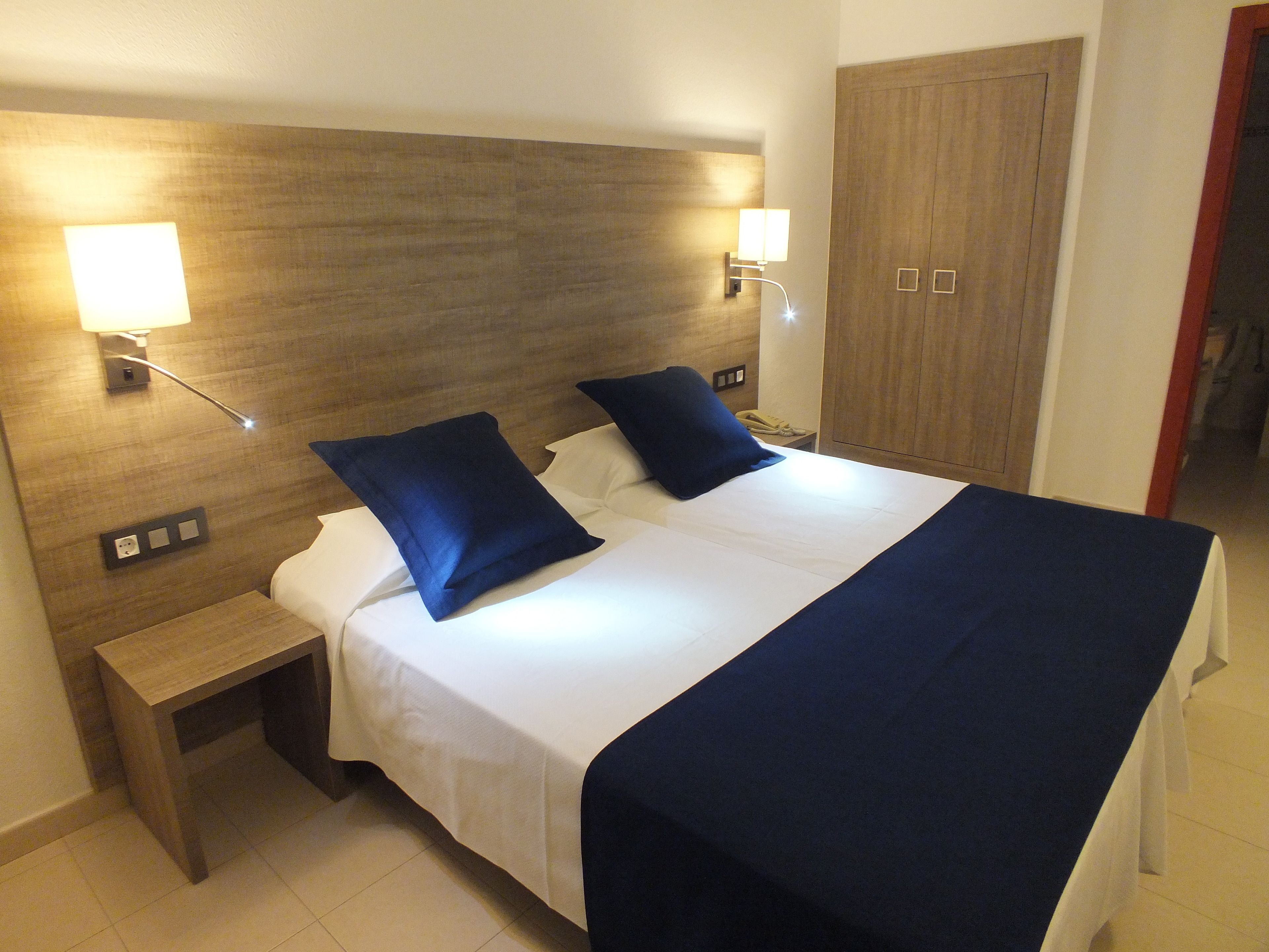 Una habitación de hotel con una cama grande, dos mesitas de noche y un armario de madera.