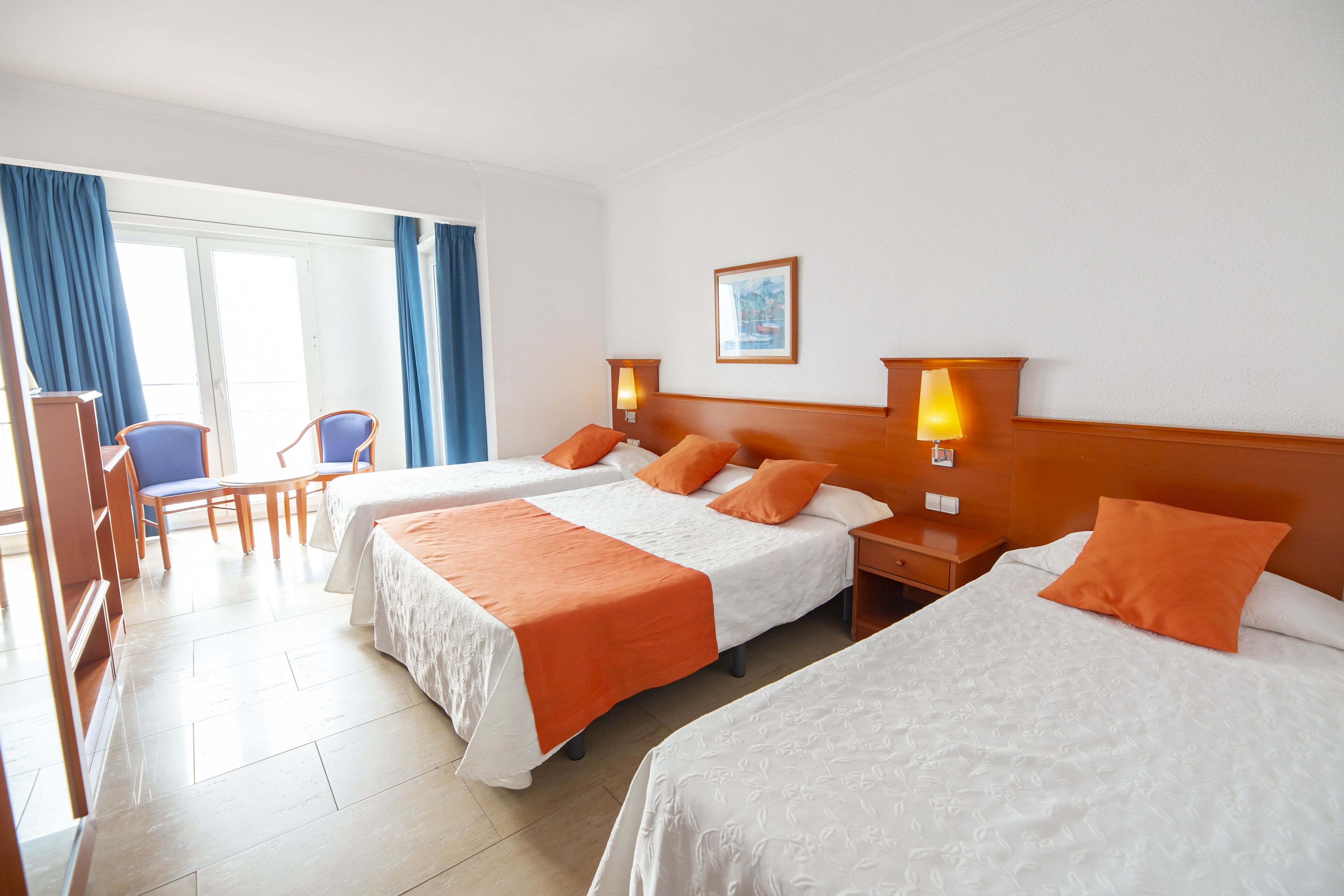 A hotel room with two beds, a desk, chairs, and a window with curtains.