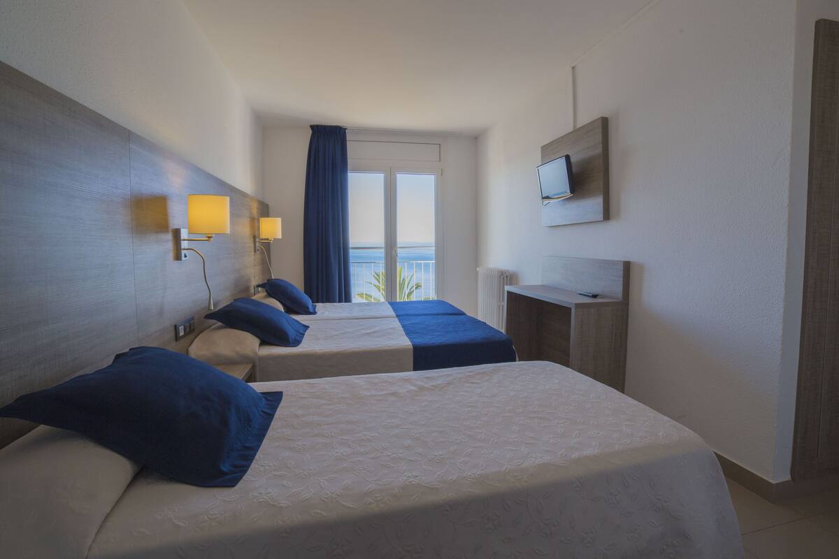 Habitación de hotel con dos camas, un televisor en la pared y vista al mar a través de la ventana.