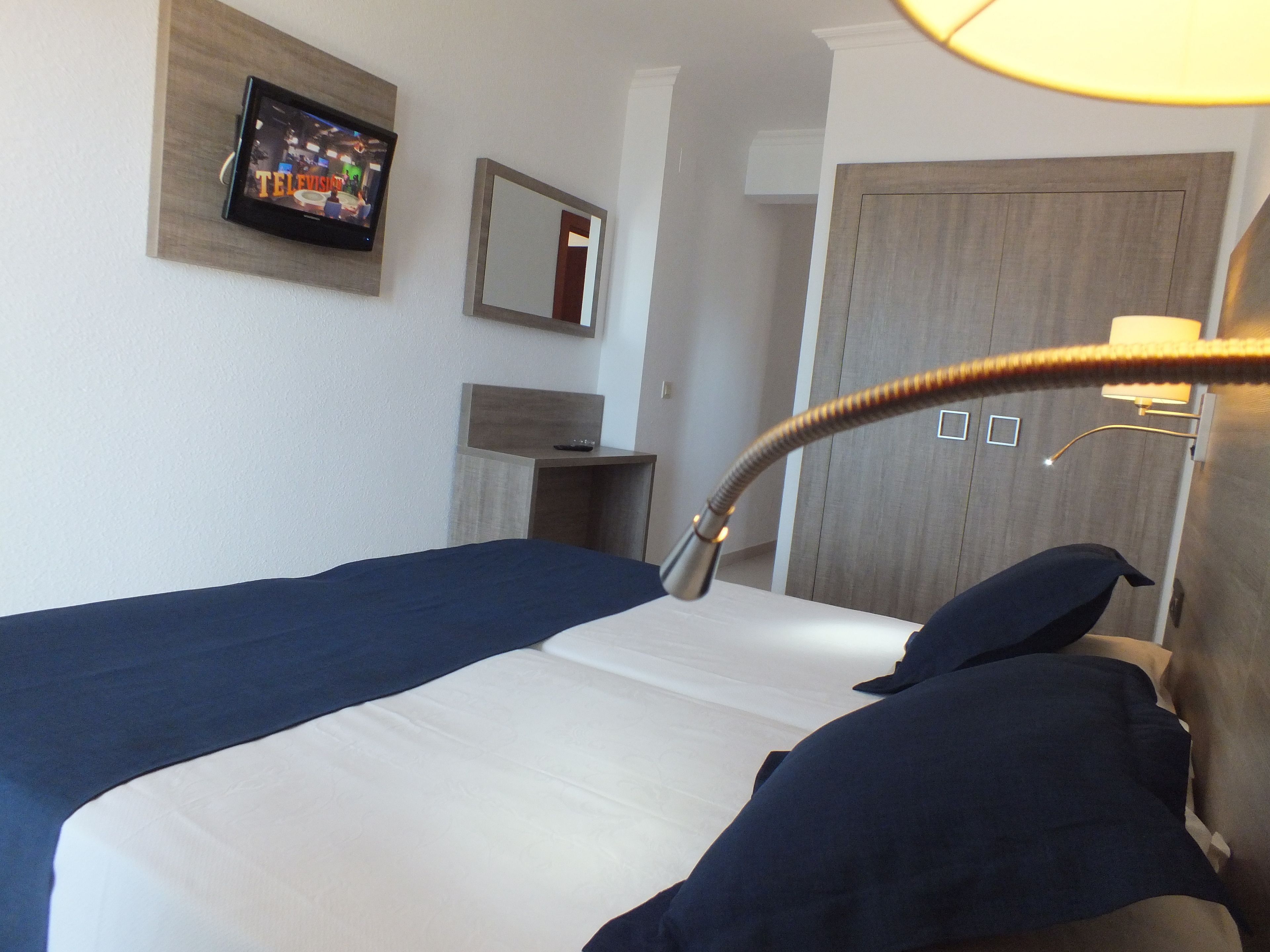 Habitación de hotel con cama, televisión montada en la pared, espejo y lámpara.