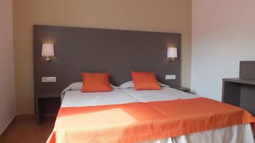 A double bed with two orange pillows, a grey headboard, and two bedside lamps.