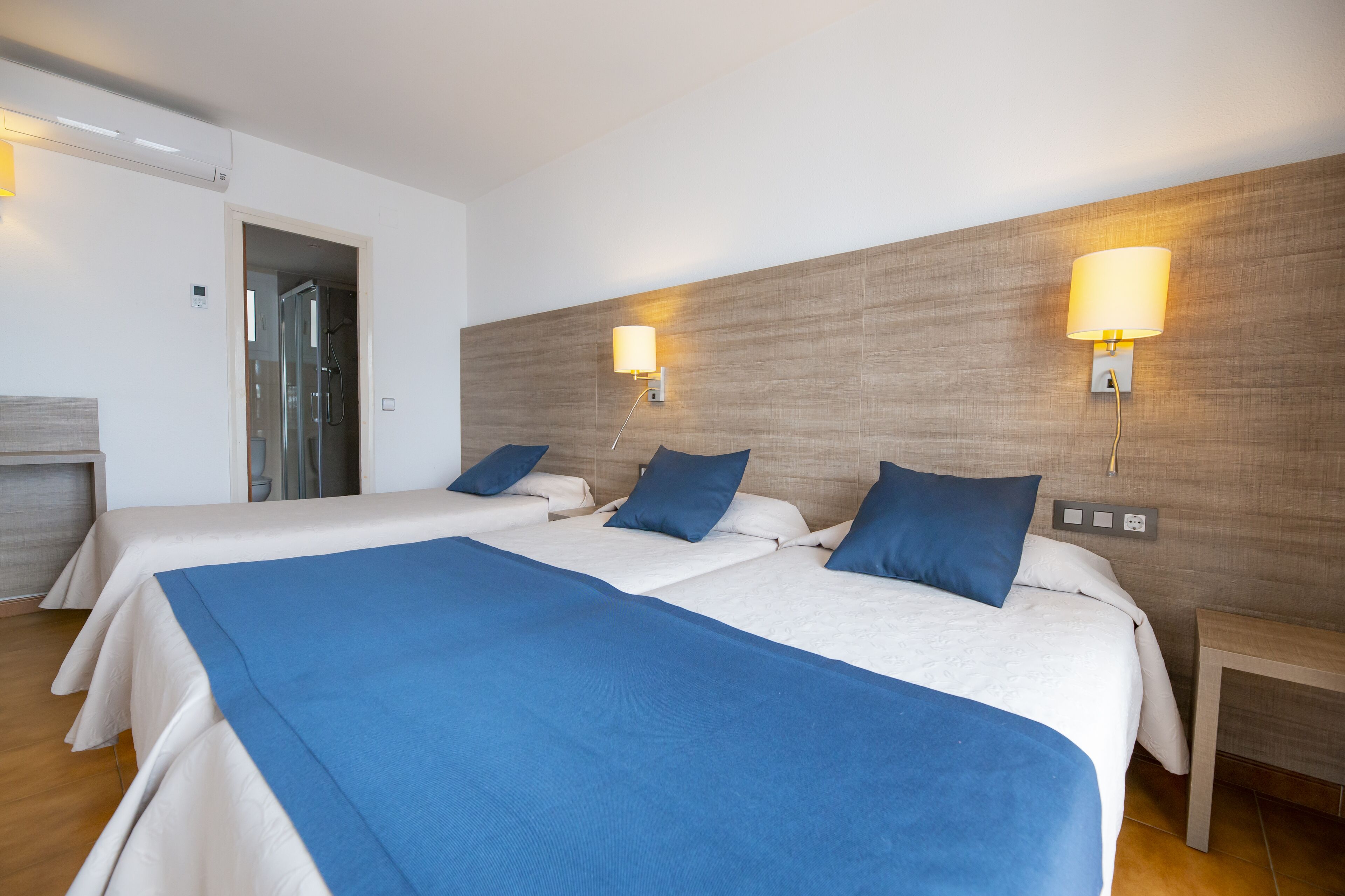 A hotel room with two beds, a wooden headboard, and a shower area.