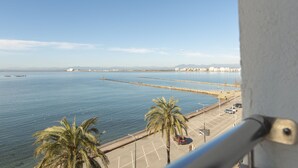 A coastal view with a clear sky, calm sea, and a parking area with palm trees. - Hotel Risech (Roses)