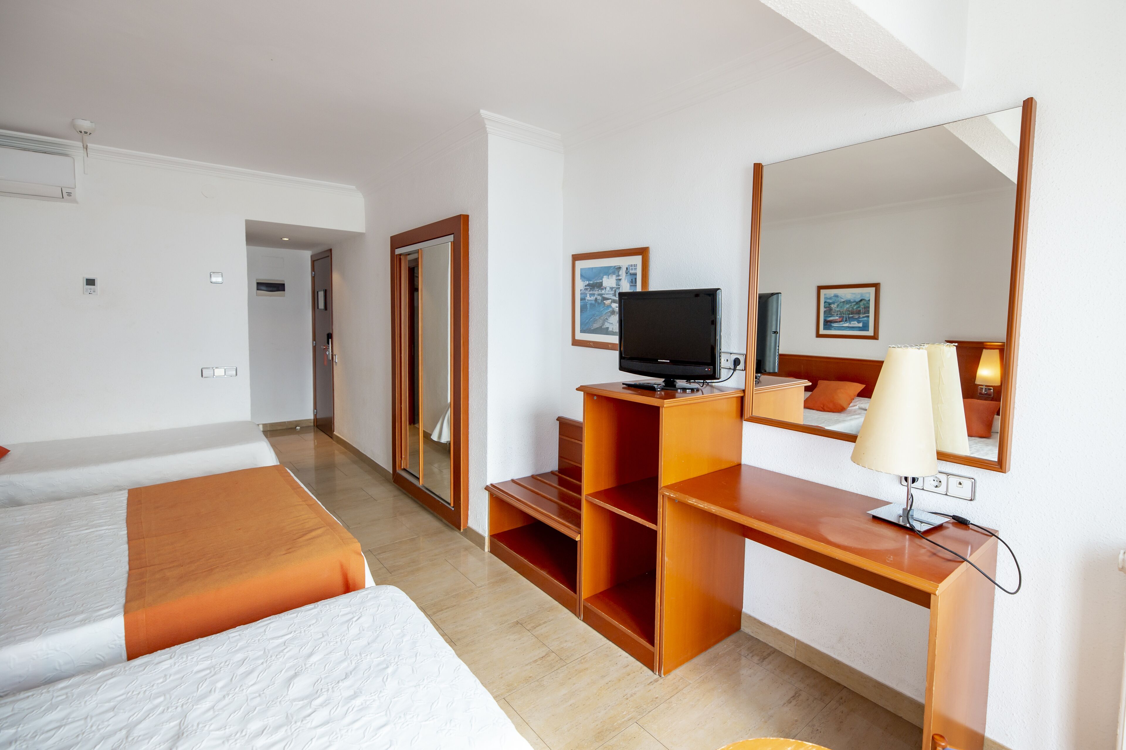 Habitación de hotel con dos camas, un escritorio de madera con televisor, un espejo y una lámpara.