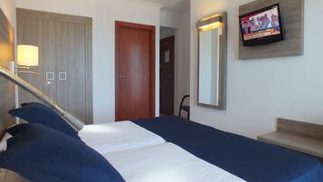 Habitación de hotel con cama, televisión, espejo y puerta.