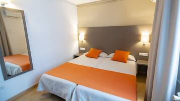 Una cama doble con ropa de cama naranja, una mesita de noche, una lámpara de pared y un espejo.