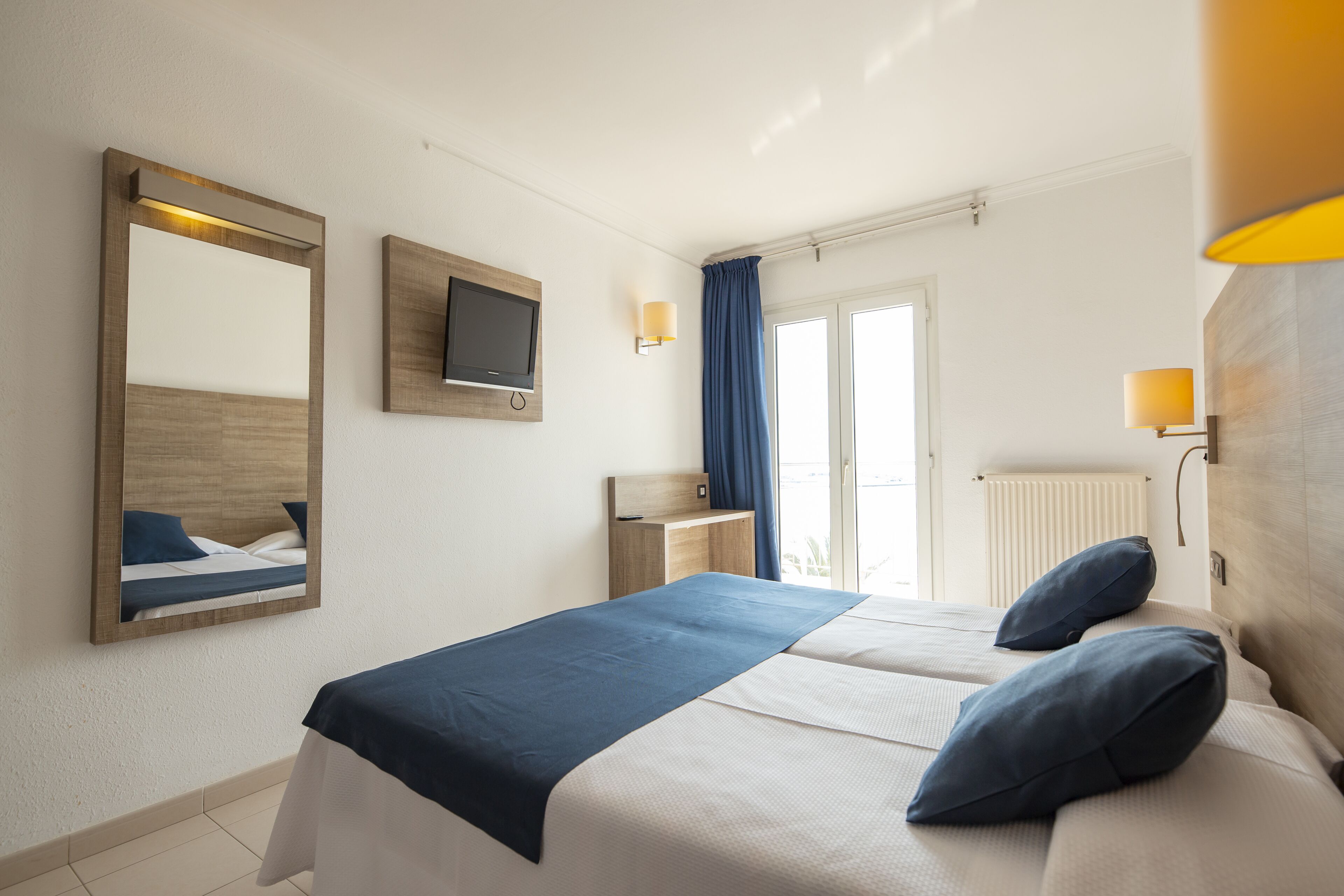 A hotel room with a bed, a TV, a desk, and a window with curtains.