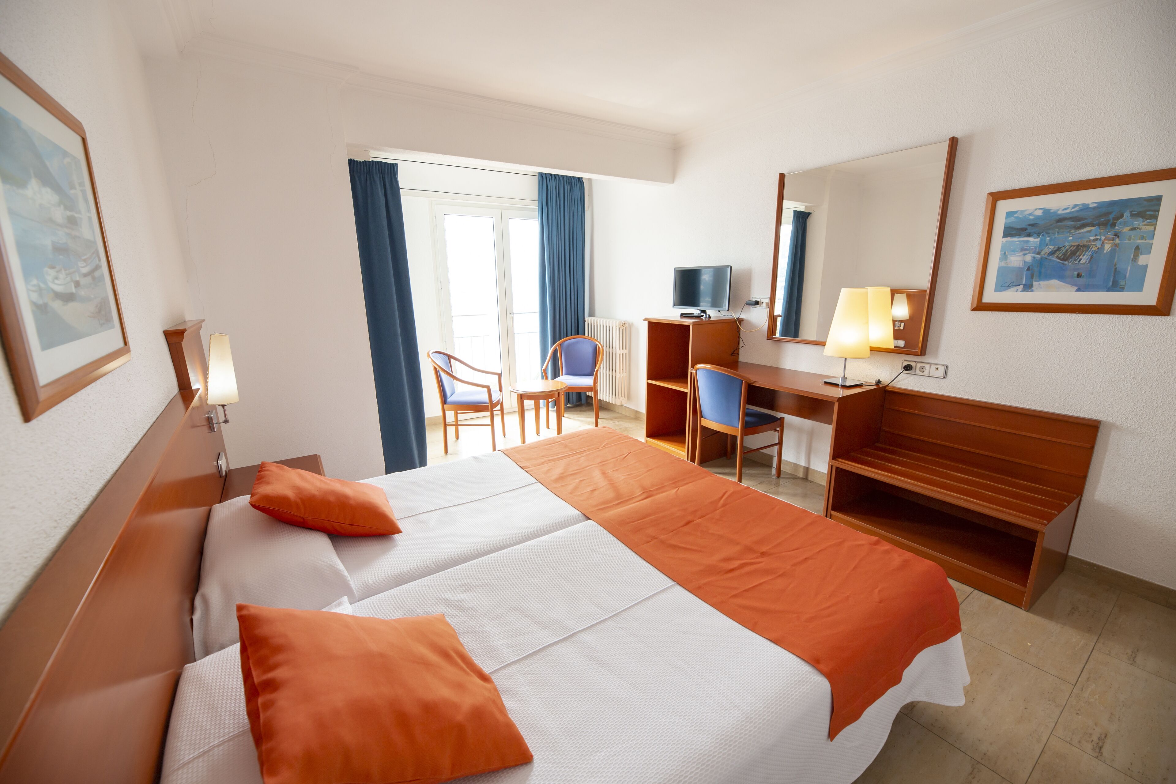 A hotel room with a large bed, a desk, a chair, a television, and a window with curtains.
