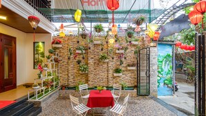 A courtyard with a red table and chairs, surrounded by potted plants and hanging lanterns. - NuNi Hoi An Homestay (Da Nang)