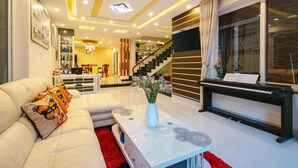 A modern living room with a white sofa, a piano, and a red rug. - NuNi Hoi An Homestay (Da Nang)