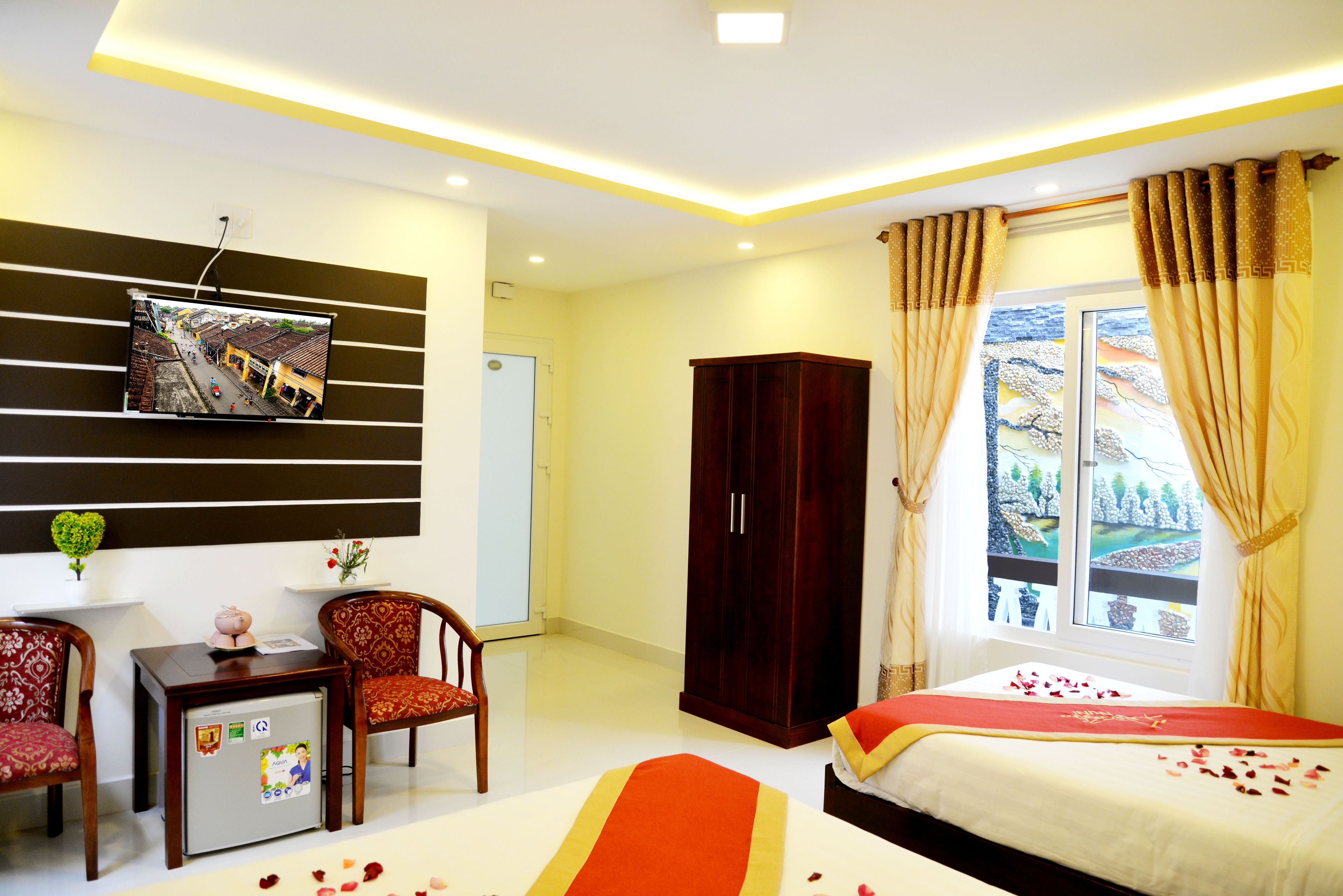 A hotel room with a bed, a desk, a wardrobe, a TV mounted on the wall, and a window with curtains.