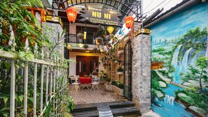 A traditional Vietnamese courtyard with a mural, a red table, and a staircase leading to a wooden door. - NuNi Hoi An Homestay (Da Nang)