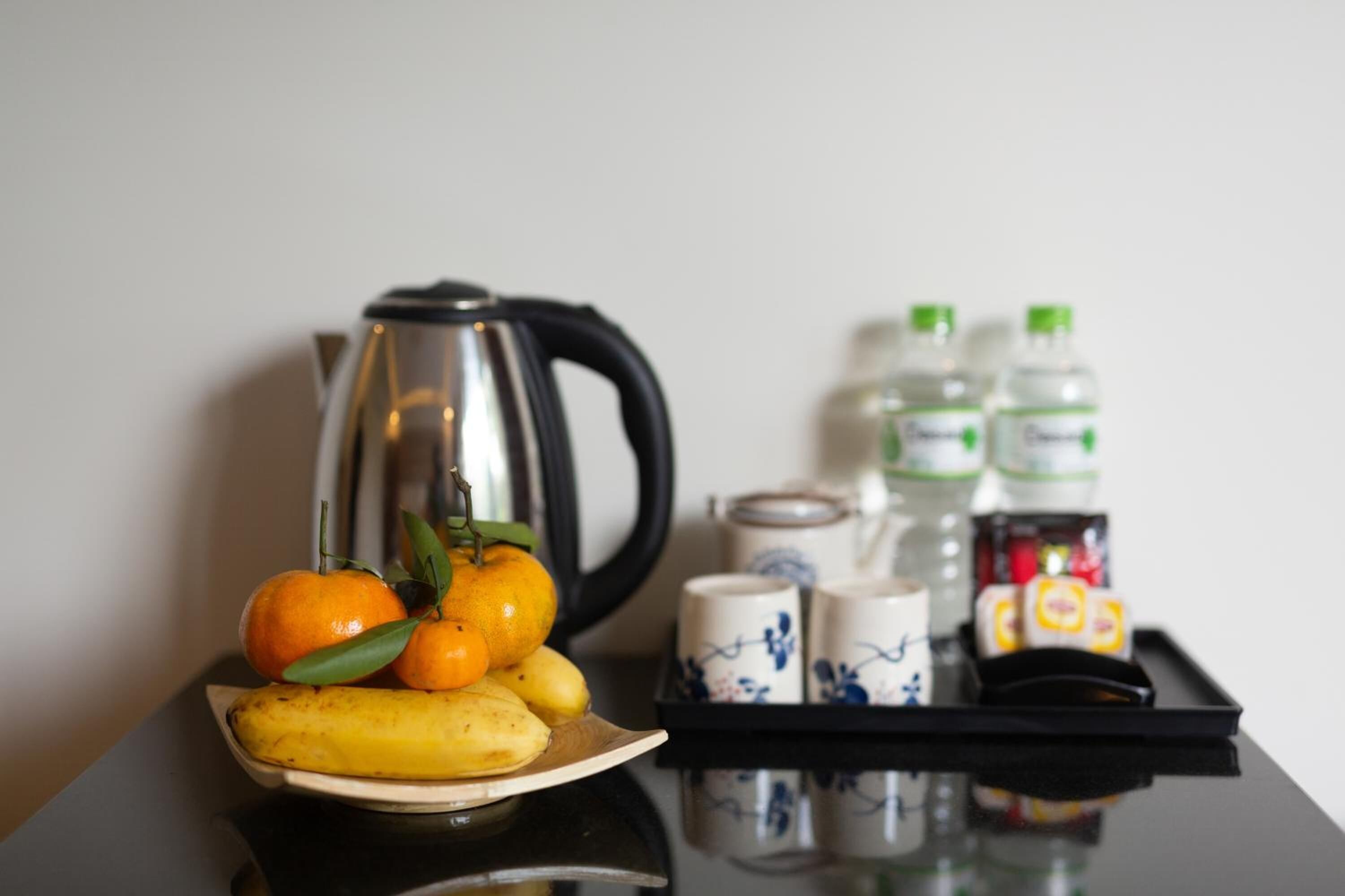 A tray with a banana, oranges, and a kettle. There are also bottles and cups on the tray.