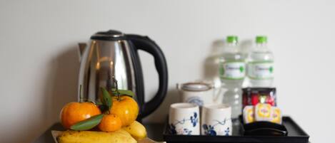A tray with a banana, oranges, and a kettle. There are also bottles and cups on the tray.