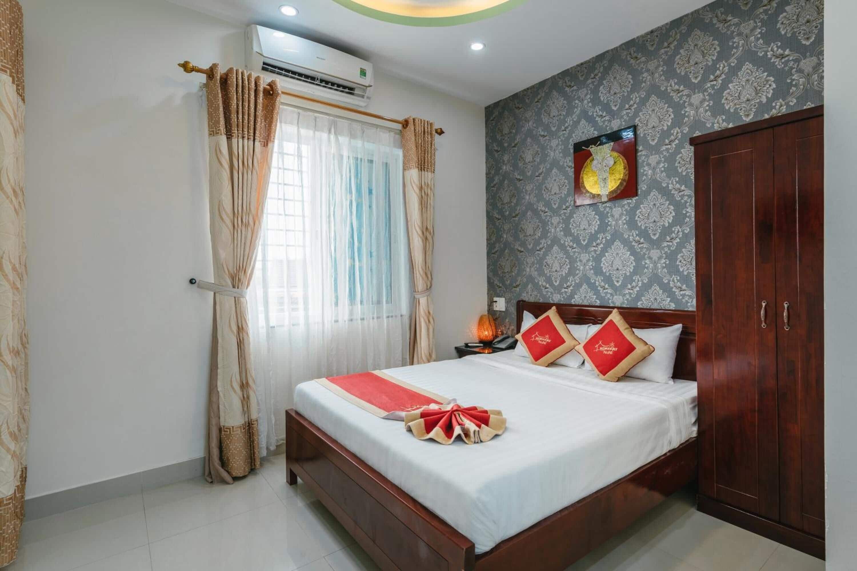 A hotel room with a bed, curtains, an air conditioner, a nightstand, and a wardrobe.